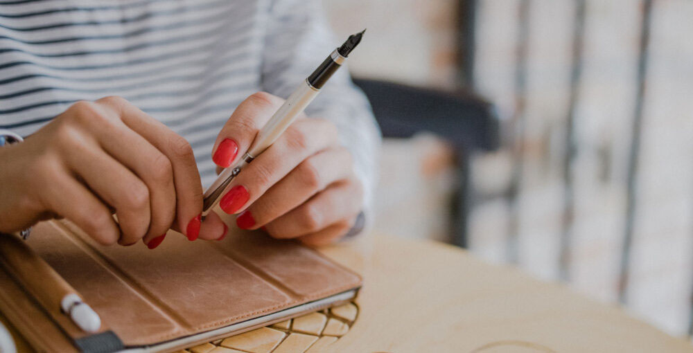 Person holding a pen above a notebook while reviewing financial records and business documents.