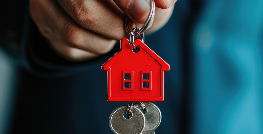 Person holding a set of house keys with a red house-shaped keyring, symbolising property ownership, home buying and residential real estate.