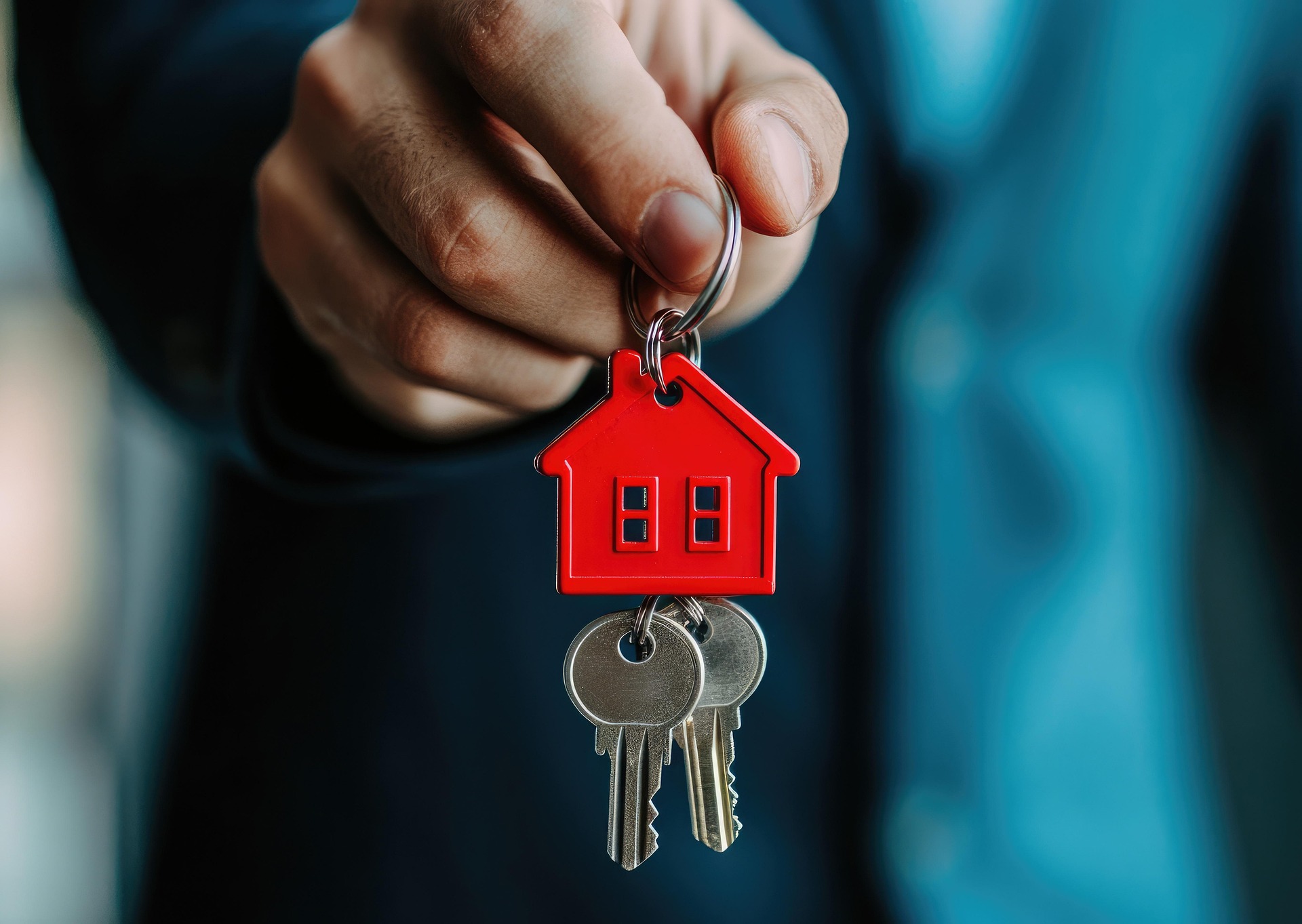 Hand holding house keys with a red house keyring